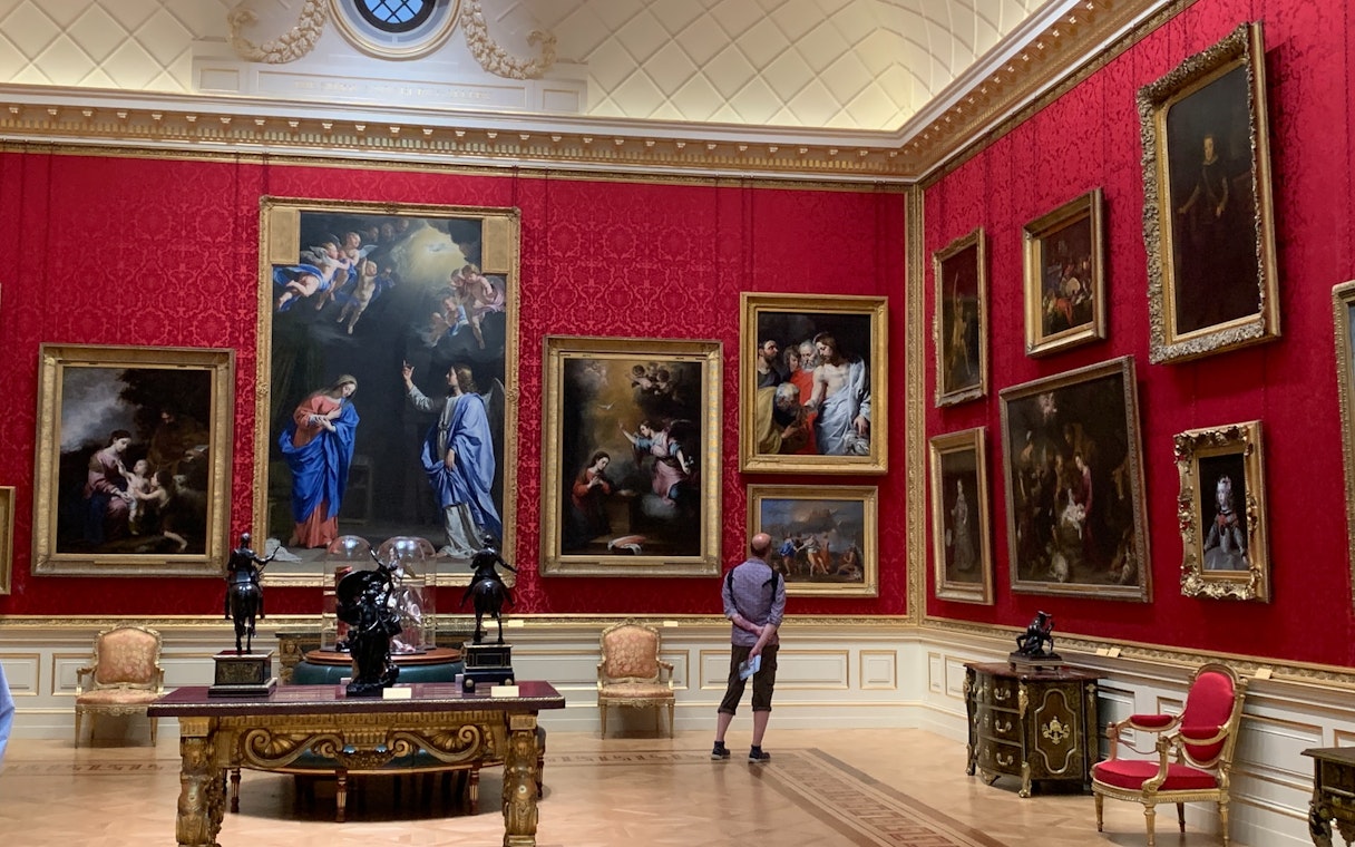 Visitor admiring Renaissance paintings in a red-walled gallery at the Uffizi Gallery, Florence.