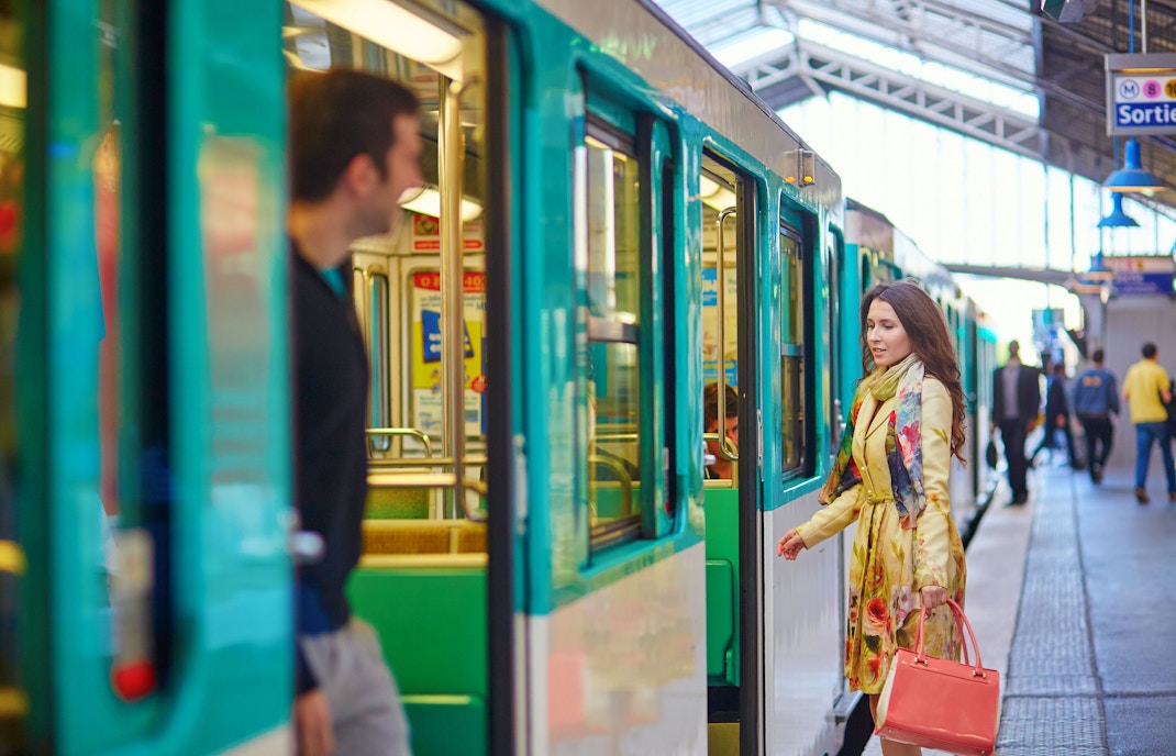 Train at Paris station with passengers boarding and cityscape in background.