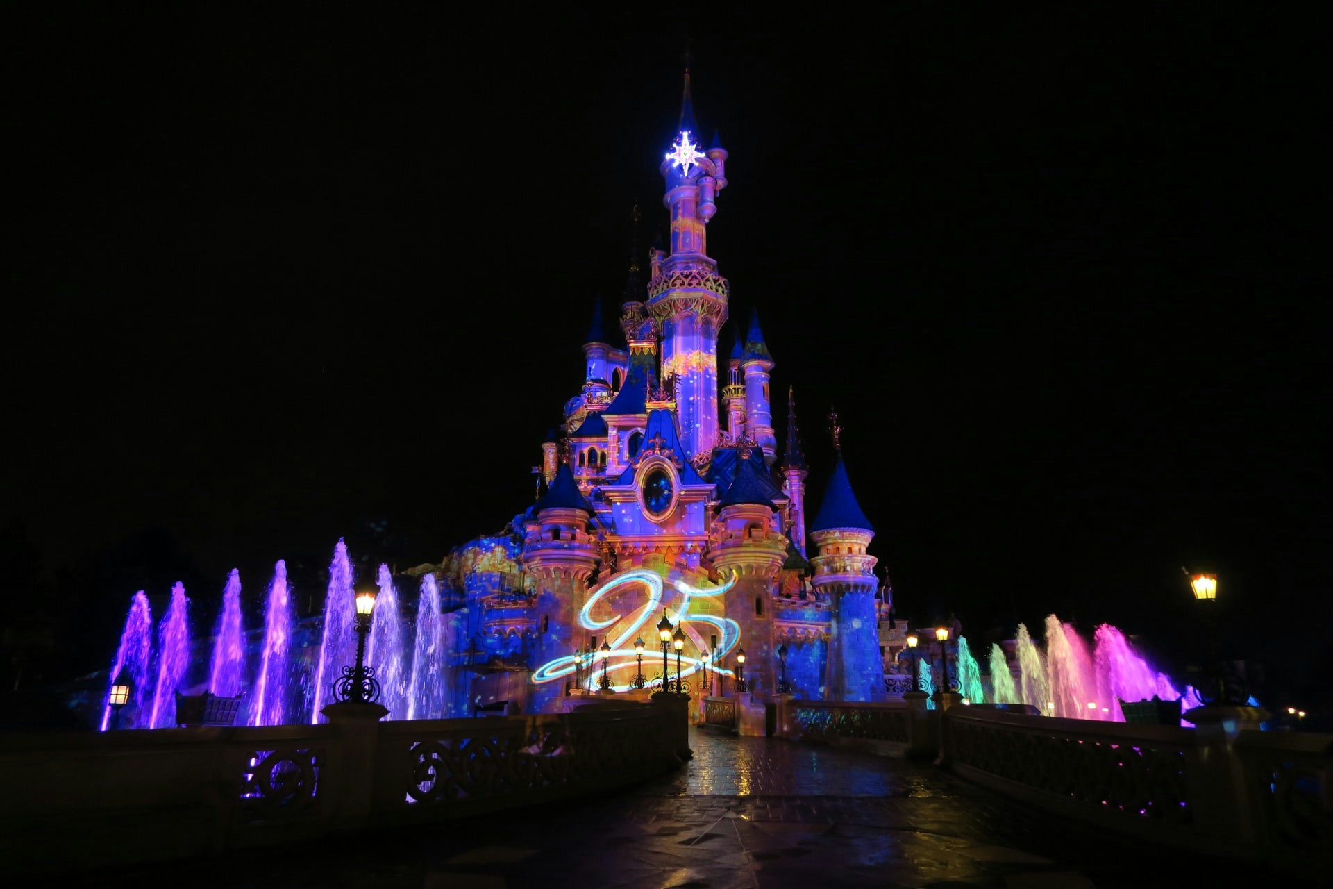 Colorful night illuminations at Disneyland Paris castle with fountains.