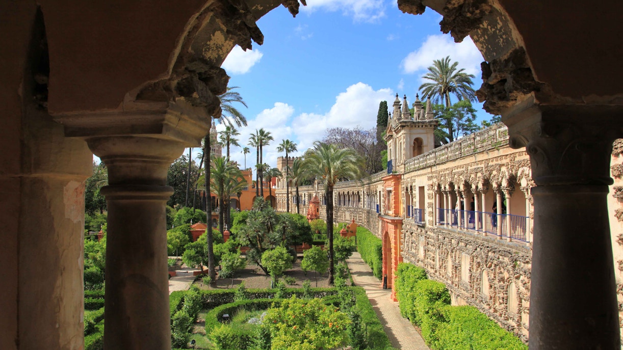 Alcazar Seville courtyard with intricate arches and lush gardens.