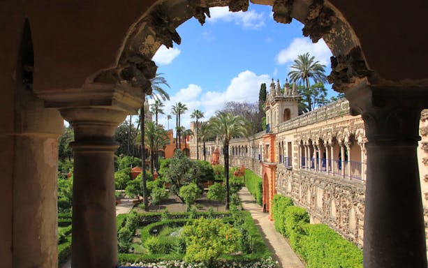 Alcazar Seville courtyard with intricate arches and lush gardens.