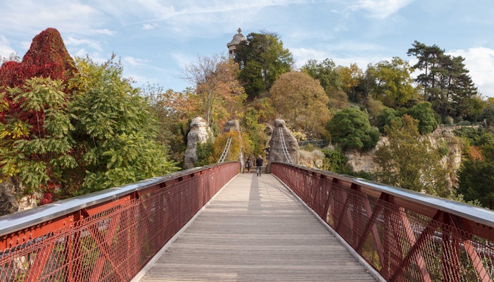 Parc des Buttes Chaumont in Paris with lush greenery, a suspension bridge, and a temple on a hilltop.