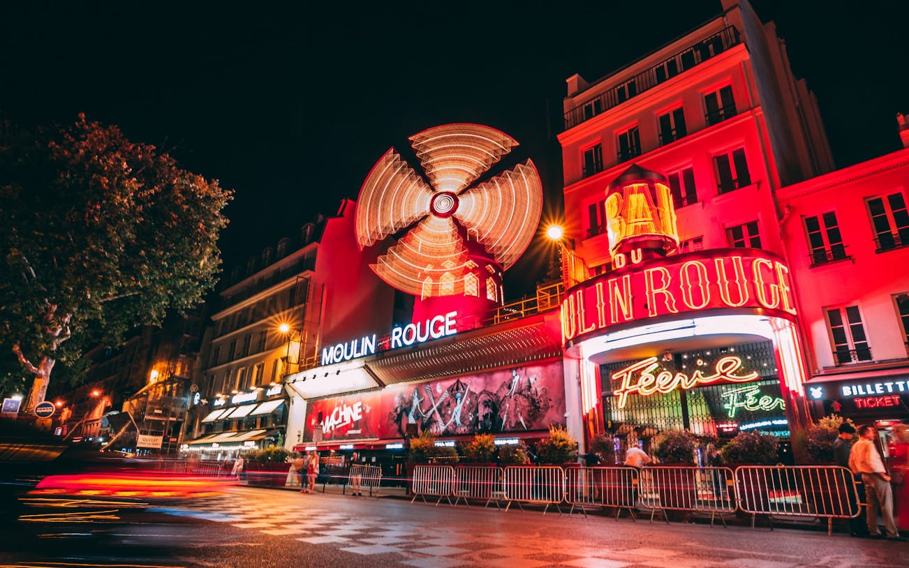 Moulin Rouge theatre exterior with illuminated windmill in Paris at night.