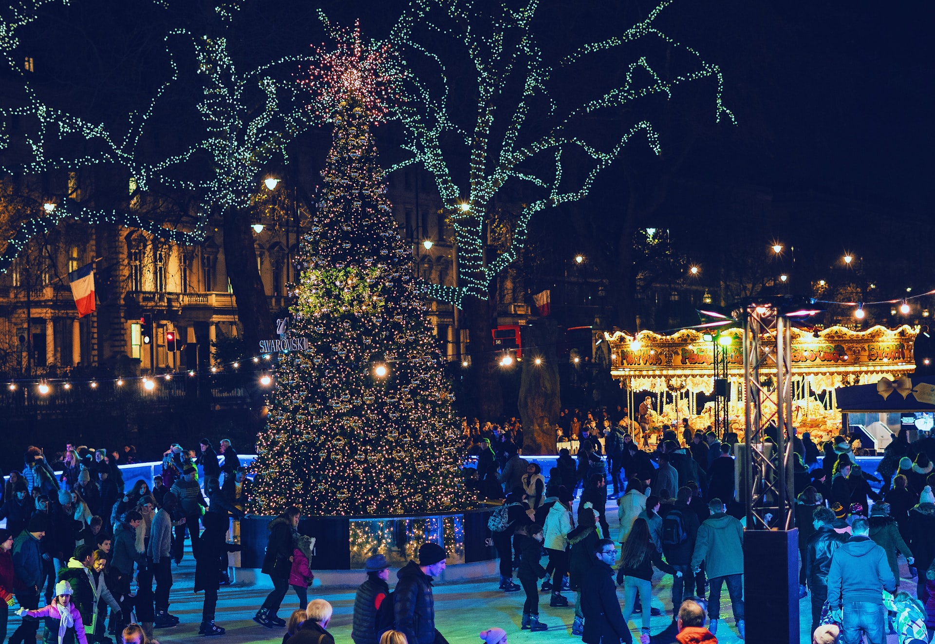 Ice skaters at Kew Gardens Christmas event with illuminated tree and carousel.