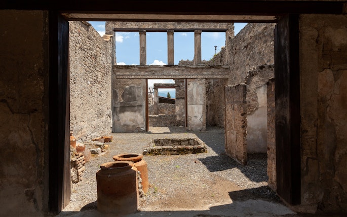 Pompeii ruins with ancient stone walls and pottery, viewed by tourists on a Rome day trip.