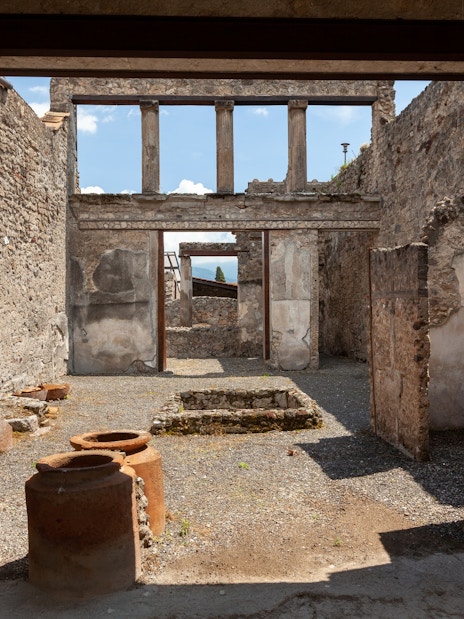 Pompeii ruins with ancient stone walls and pottery, viewed by tourists on a Rome day trip.