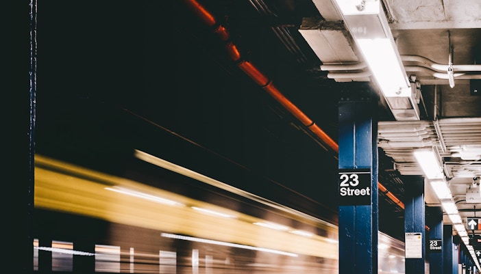subway station platform in NYC with a train in motion.