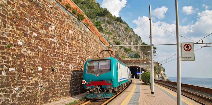 Train approaching a tunnel at Cinque Terre station, Italy, with coastal views.