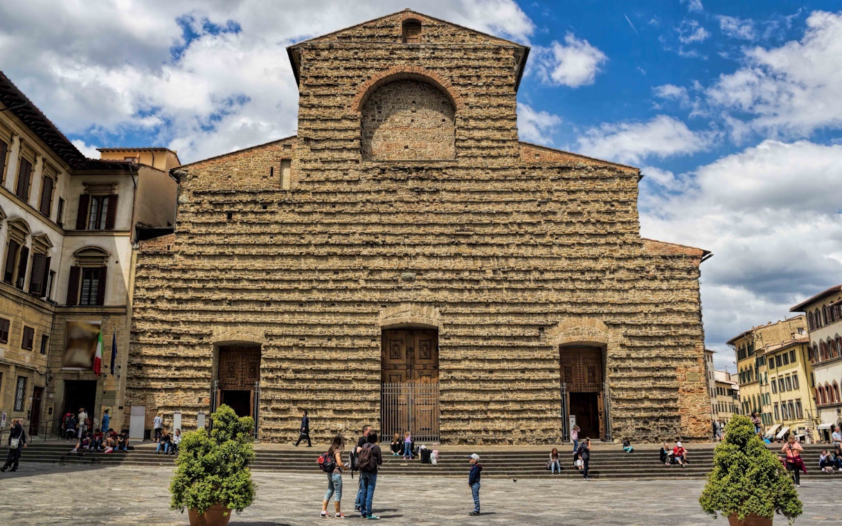 Visitors in front of San Lorenzo Church's stone facade in Florence on a sunny day.