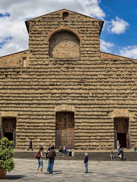 Visitors in front of San Lorenzo Church's stone facade in Florence on a sunny day.