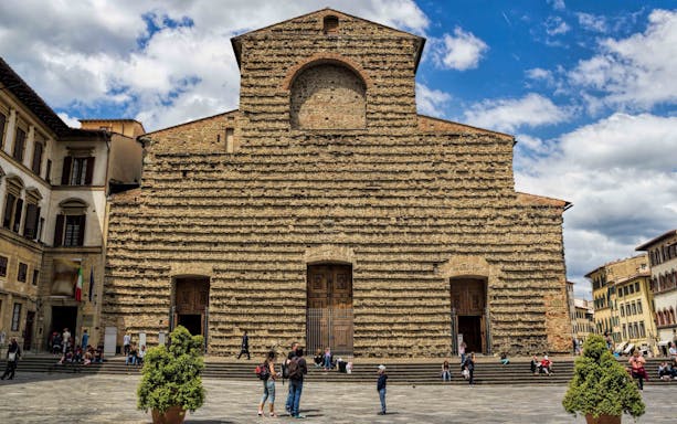 Visitors in front of San Lorenzo Church's stone facade in Florence on a sunny day.