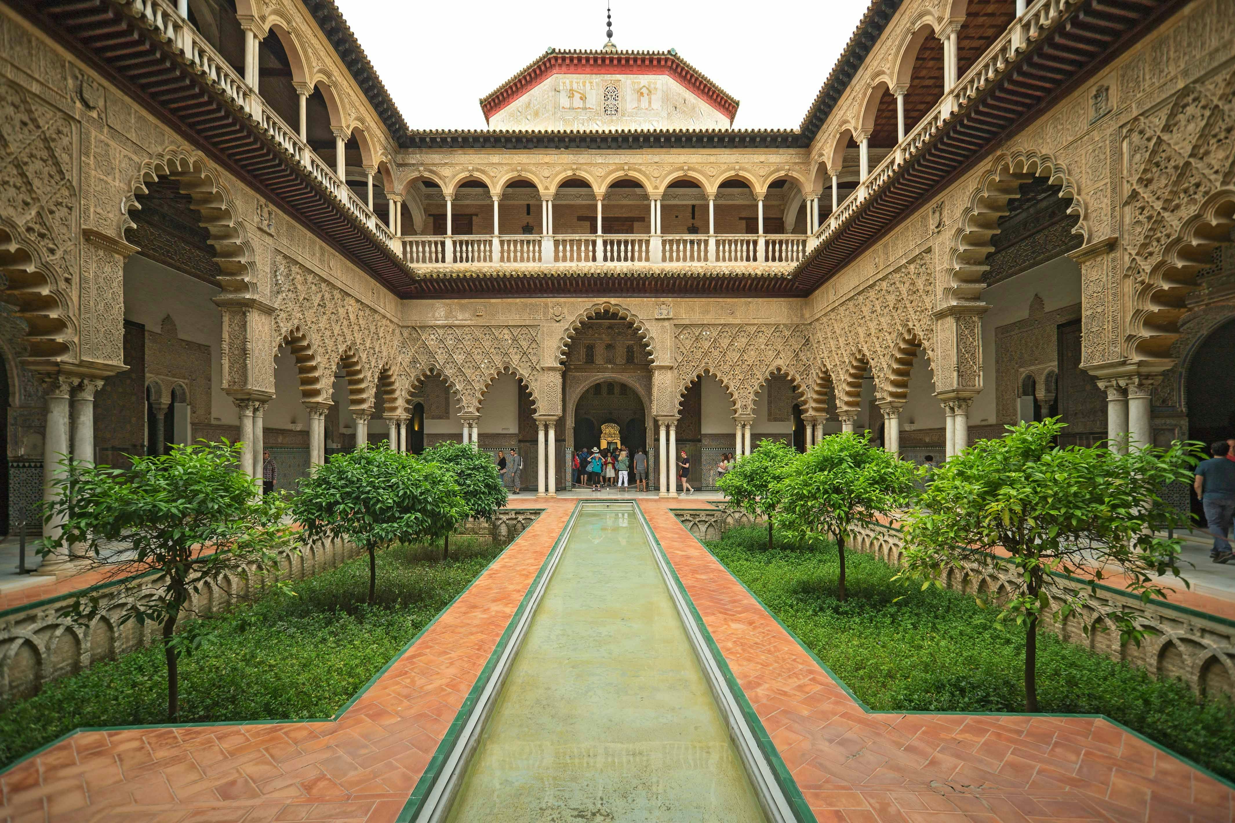 Royal Alcazar of Seville courtyard with intricate arches and lush gardens.