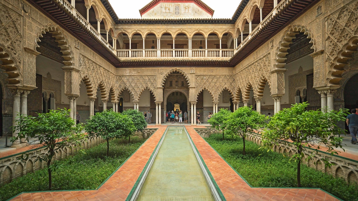 Royal Alcazar of Seville courtyard with intricate arches and lush gardens.