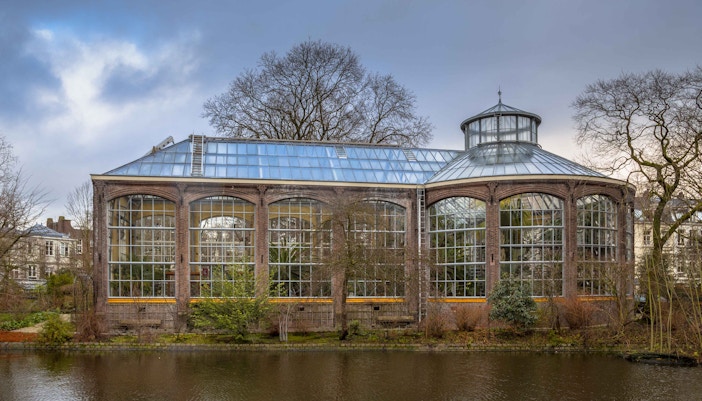 Hortus Botanicus Amsterdam greenhouse by a canal, showcasing its glass architecture.