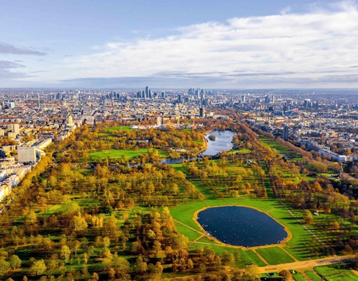 Aerial view of Hyde Park in London with Serpentine Lake and city skyline.
