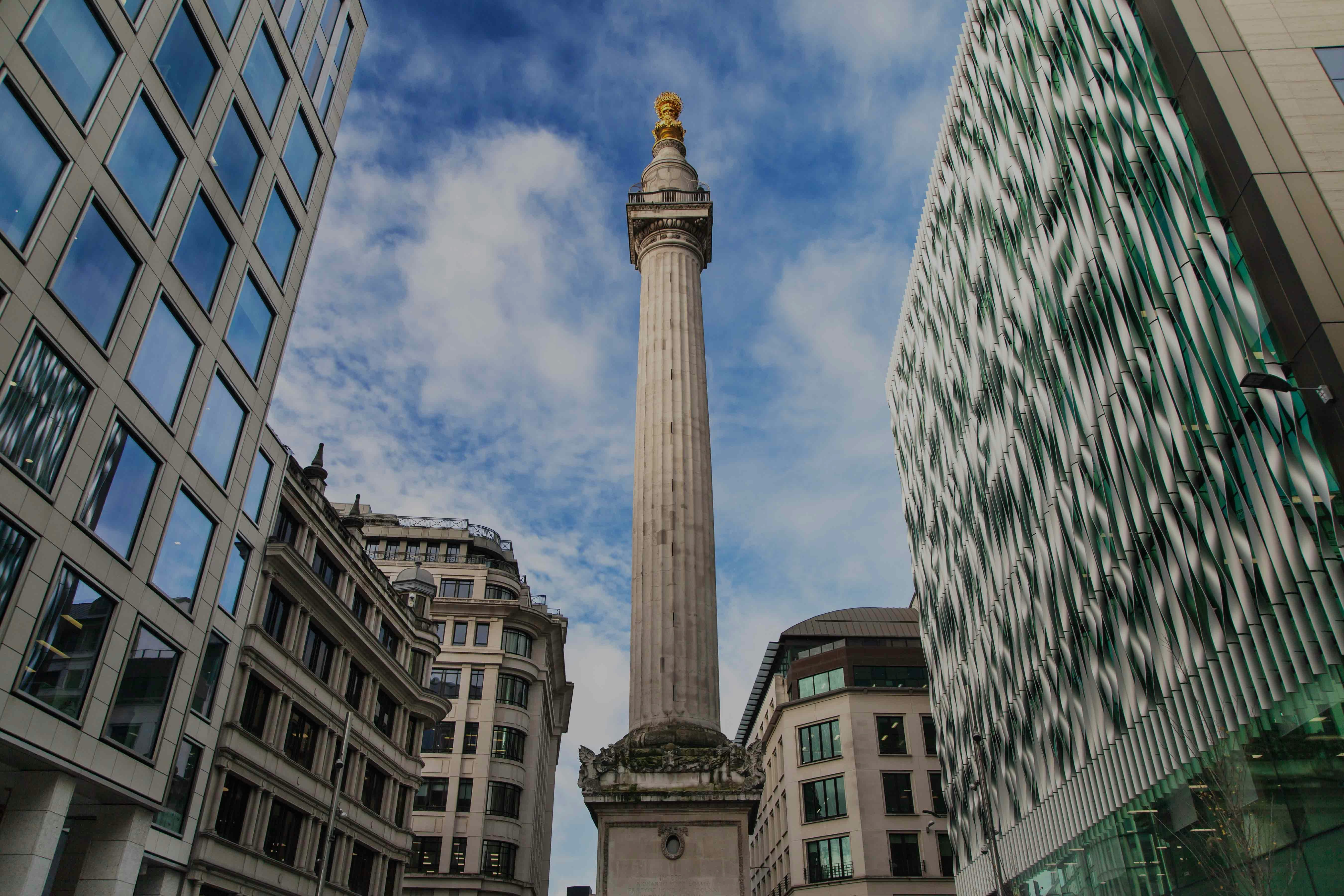 Monument to the Great Fire of London surrounded by modern buildings under a blue sky.