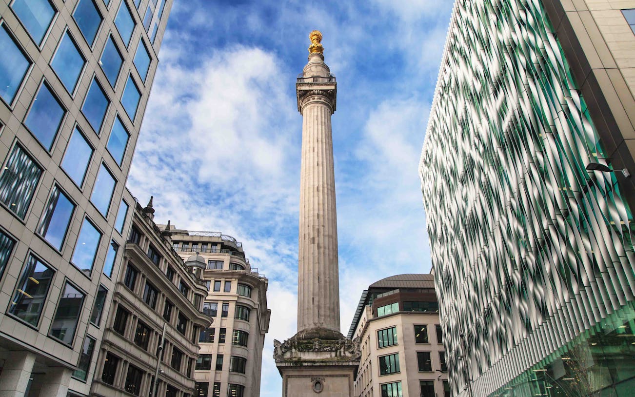 Monument to the Great Fire of London surrounded by modern buildings under a blue sky.
