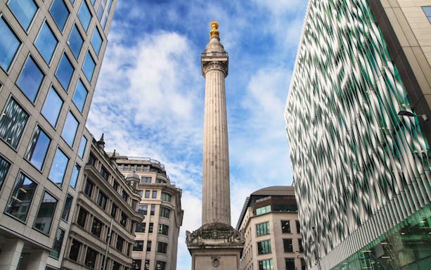 Monument to the Great Fire of London surrounded by modern buildings under a blue sky.