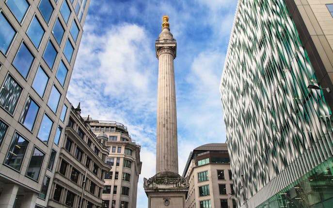 Monument to the Great Fire of London surrounded by modern buildings under a blue sky.