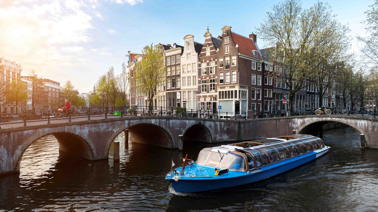 Canal cruise boat passing under a bridge in Amsterdam with historic buildings in the background.
