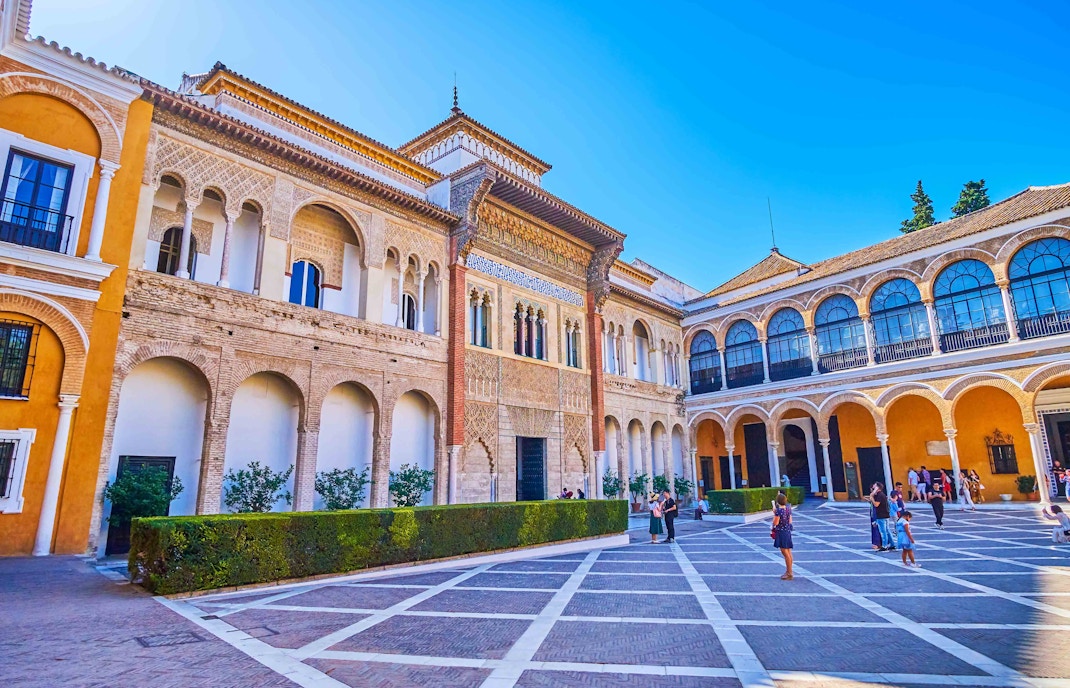 Alcazar Seville courtyard with intricate arches and lush gardens.