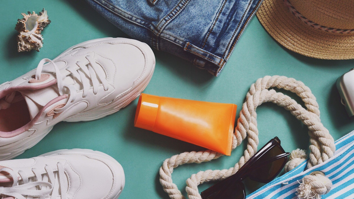 Sneakers, denim shorts, sunscreen, sunglasses, and a hat for packing in Singapore in July.