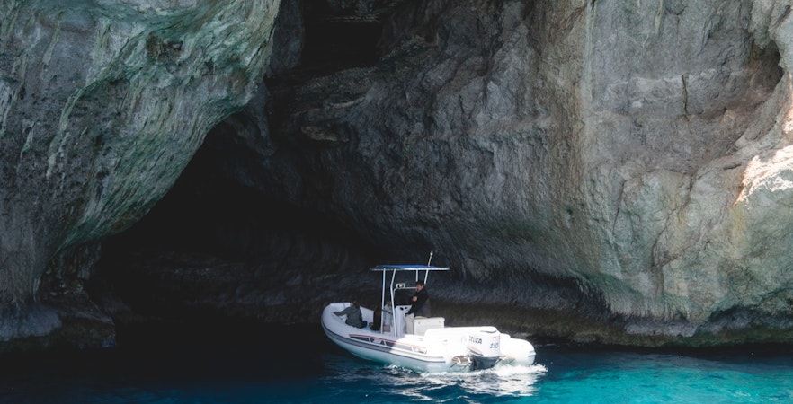 Boat entering a blue cave with clear turquoise water.