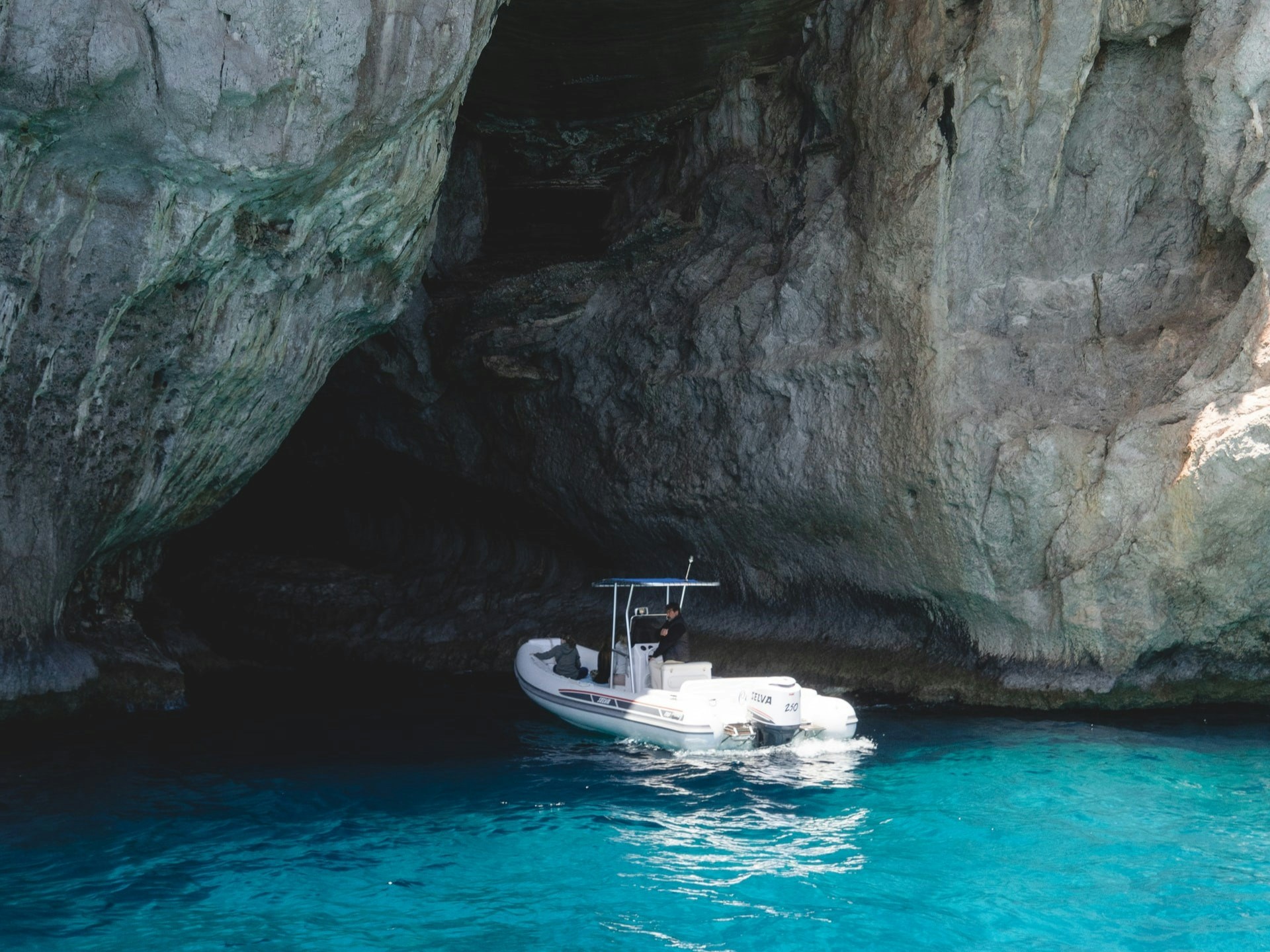 Boat entering a blue cave with clear turquoise water.