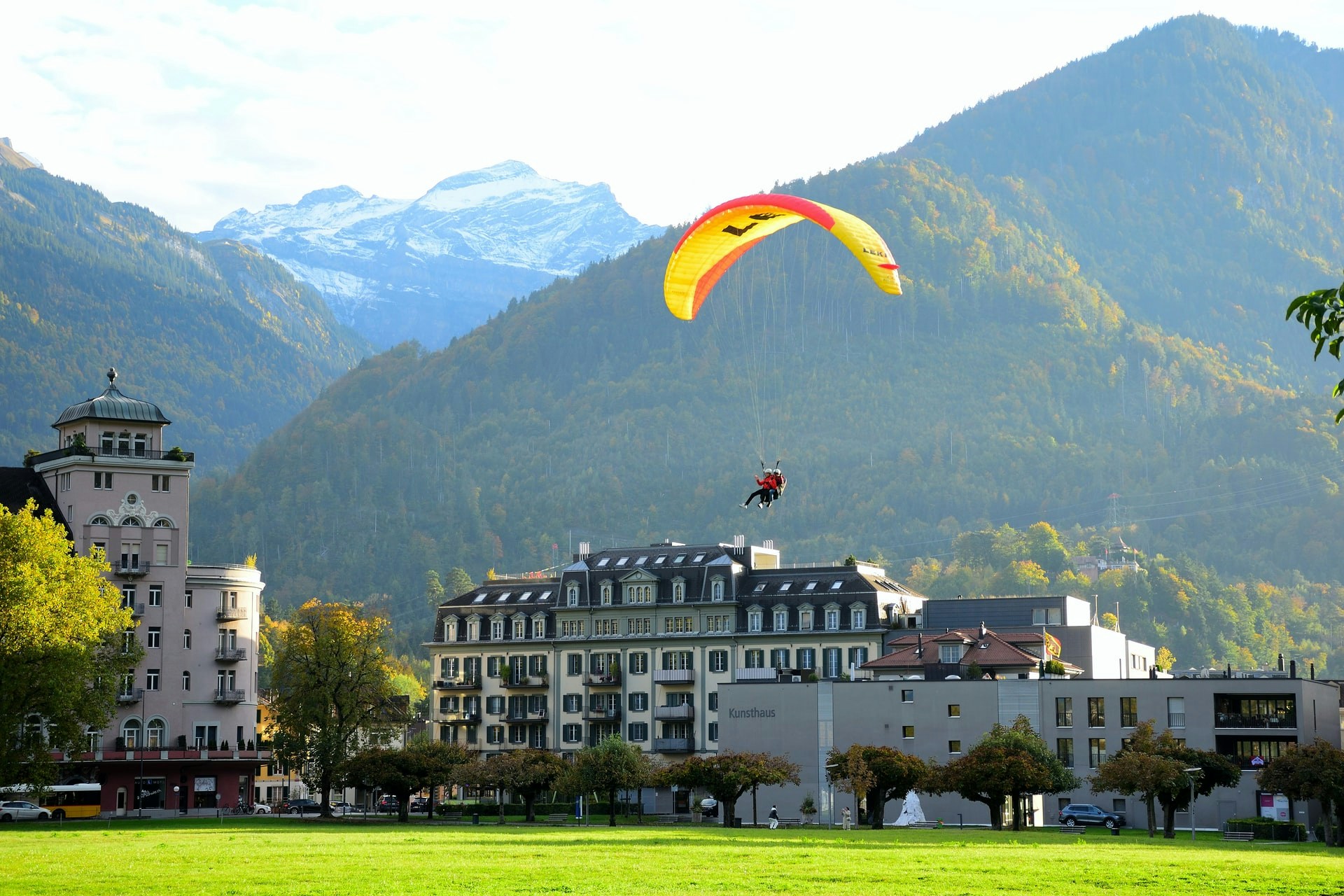 Paragliders soaring over Interlaken with Swiss Alps in the background.