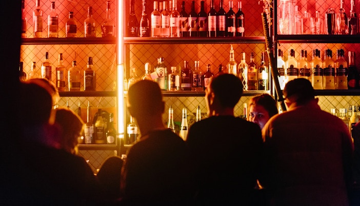 Patrons at a bar in Candelaria pub with bottles on shelves.
