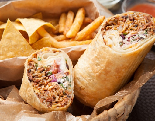 Burrito with rice and vegetables, served with fries and tortilla chips in London street food setting.