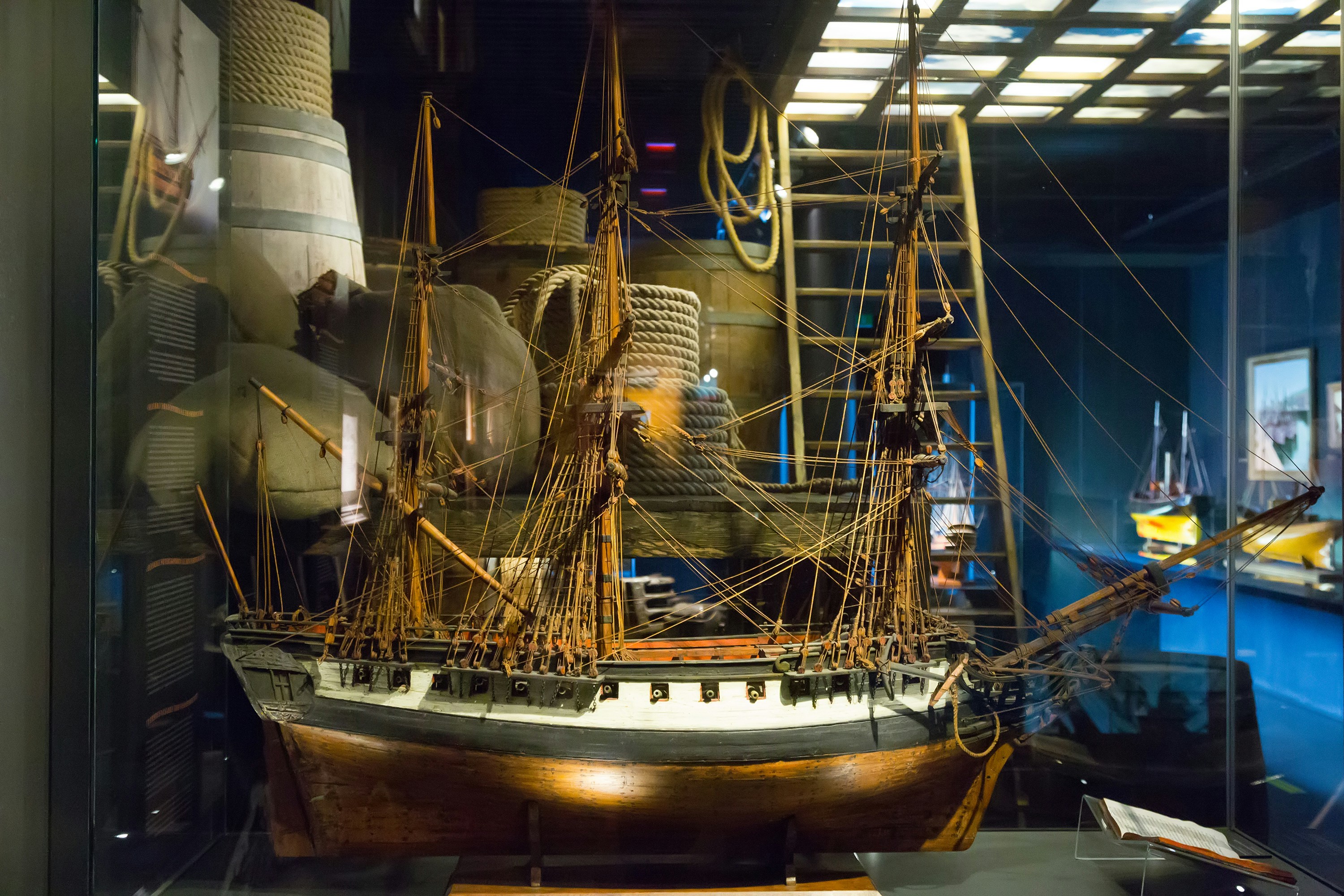 Modellschiffausstellung im Aquarium von San Sebastián mit nautischen Seilen und Fässern im Hintergrund.