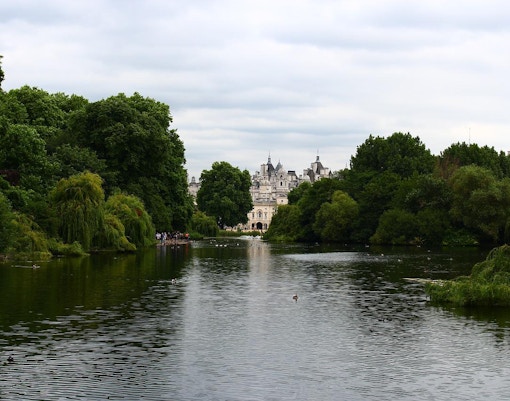 Hyde Park in London with people enjoying a sunny day by the Serpentine Lake.