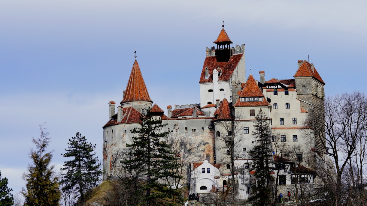 Bran Castle in Romania with red-tiled roofs and stone walls surrounded by trees.