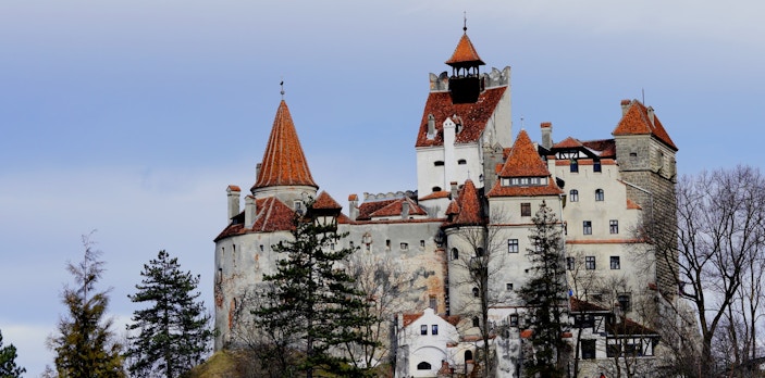 Bran Castle in Romania with red-tiled roofs and stone walls surrounded by trees.