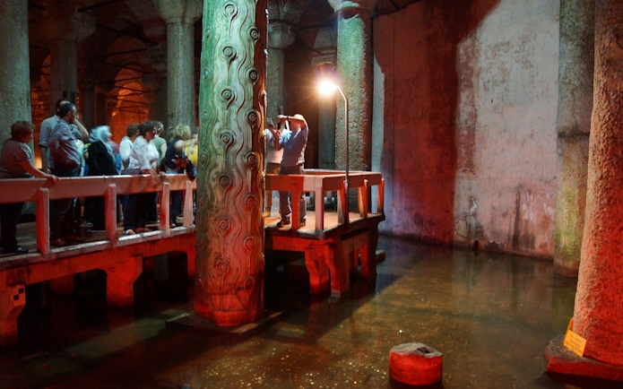 Visitors exploring the Basilica Cistern in Istanbul, viewing ancient columns and reflections in water.