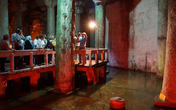 Visitors exploring the Basilica Cistern in Istanbul, viewing ancient columns and reflections in water.