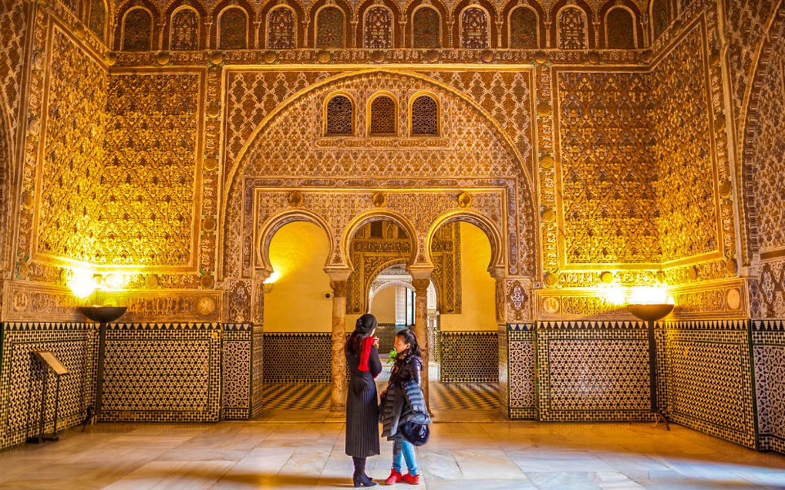 Royal Alcazar of Seville courtyard with intricate arches and lush gardens.
