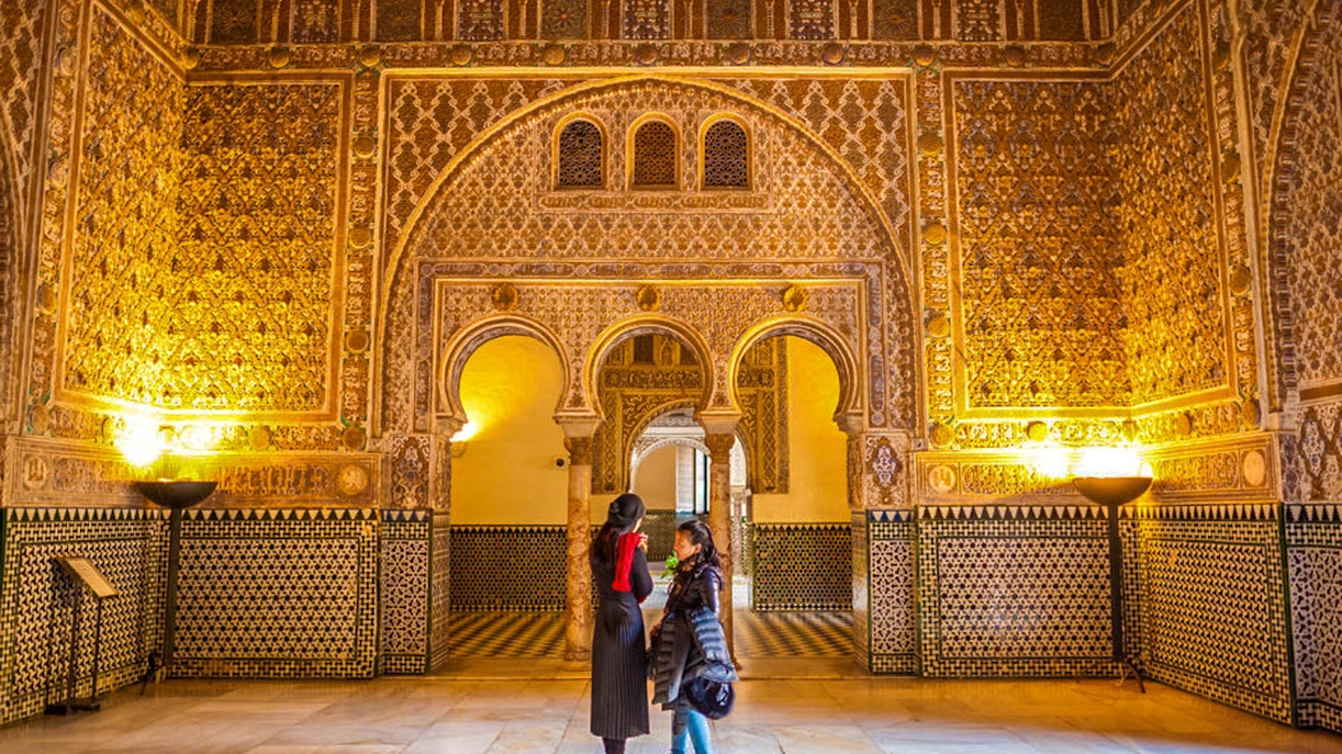 Royal Alcazar of Seville courtyard with intricate arches and lush gardens.