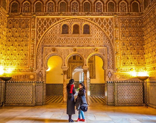 Royal Alcazar of Seville courtyard with intricate arches and lush gardens.