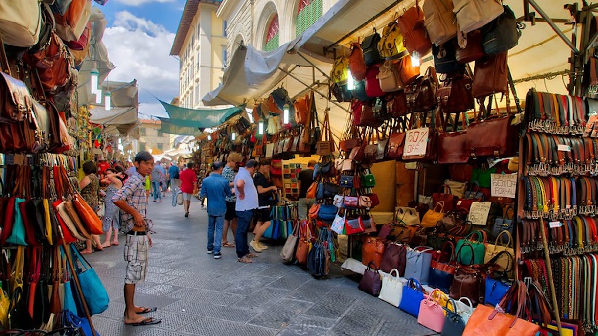 San Lorenzo Market stalls with leather bags and shoppers in Florence, Italy.