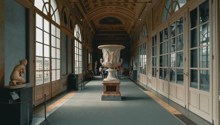 Visitors meandering through an exhibition hall at the Uffizi Gallery, surrounded by classical sculptures and bathed in natural light