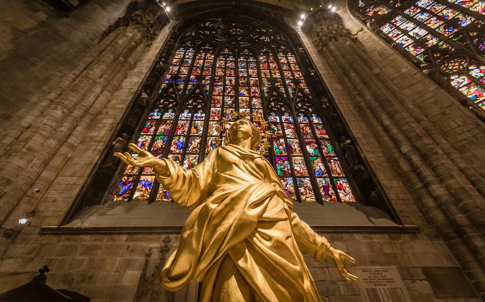 Golden statue of Madonnina inside Milan Cathedral with stained glass windows.