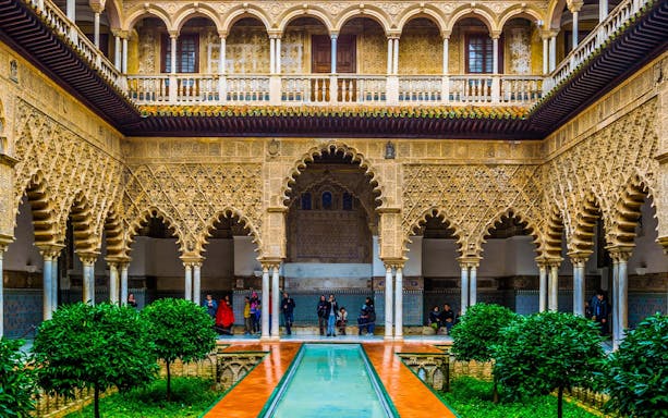 Alcazar of Seville courtyard with intricate arches and reflecting pool.
