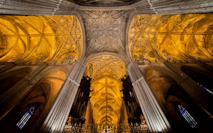 Seville Cathedral interior with ornate Gothic ceiling and columns.