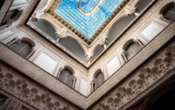 Alcazar of Seville courtyard with intricate arches and lush gardens.