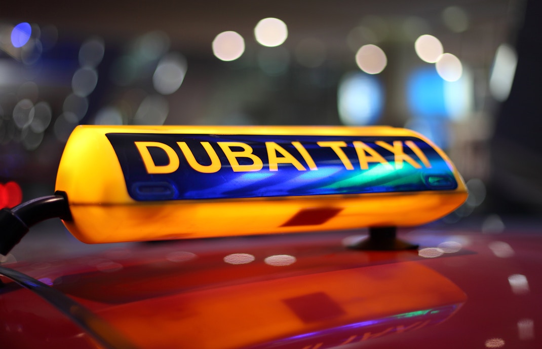 Dubai taxi driving through city streets with skyscrapers in the background.