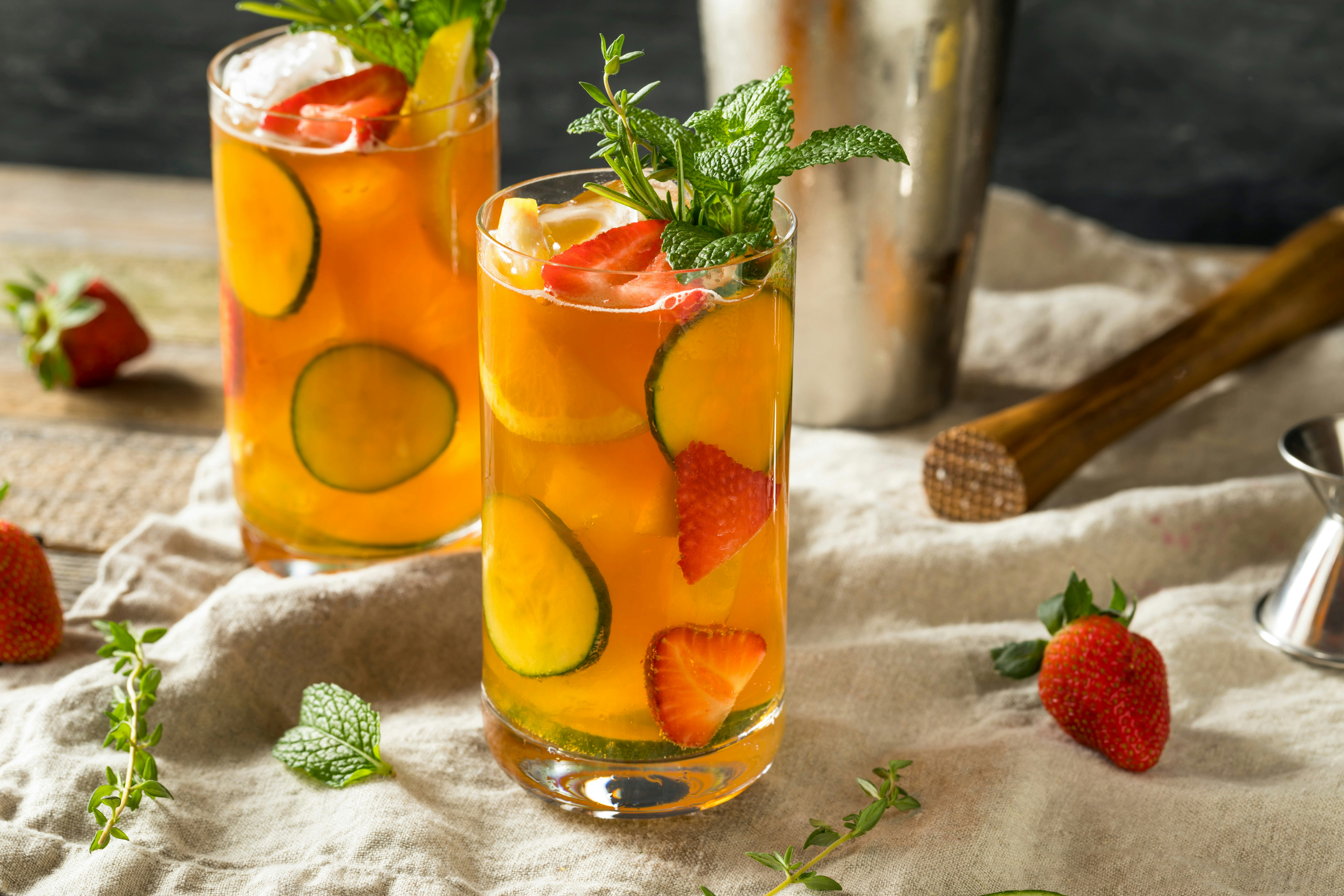 Pimm's Cup cocktail with fresh fruit garnish in a glass on a wooden table.