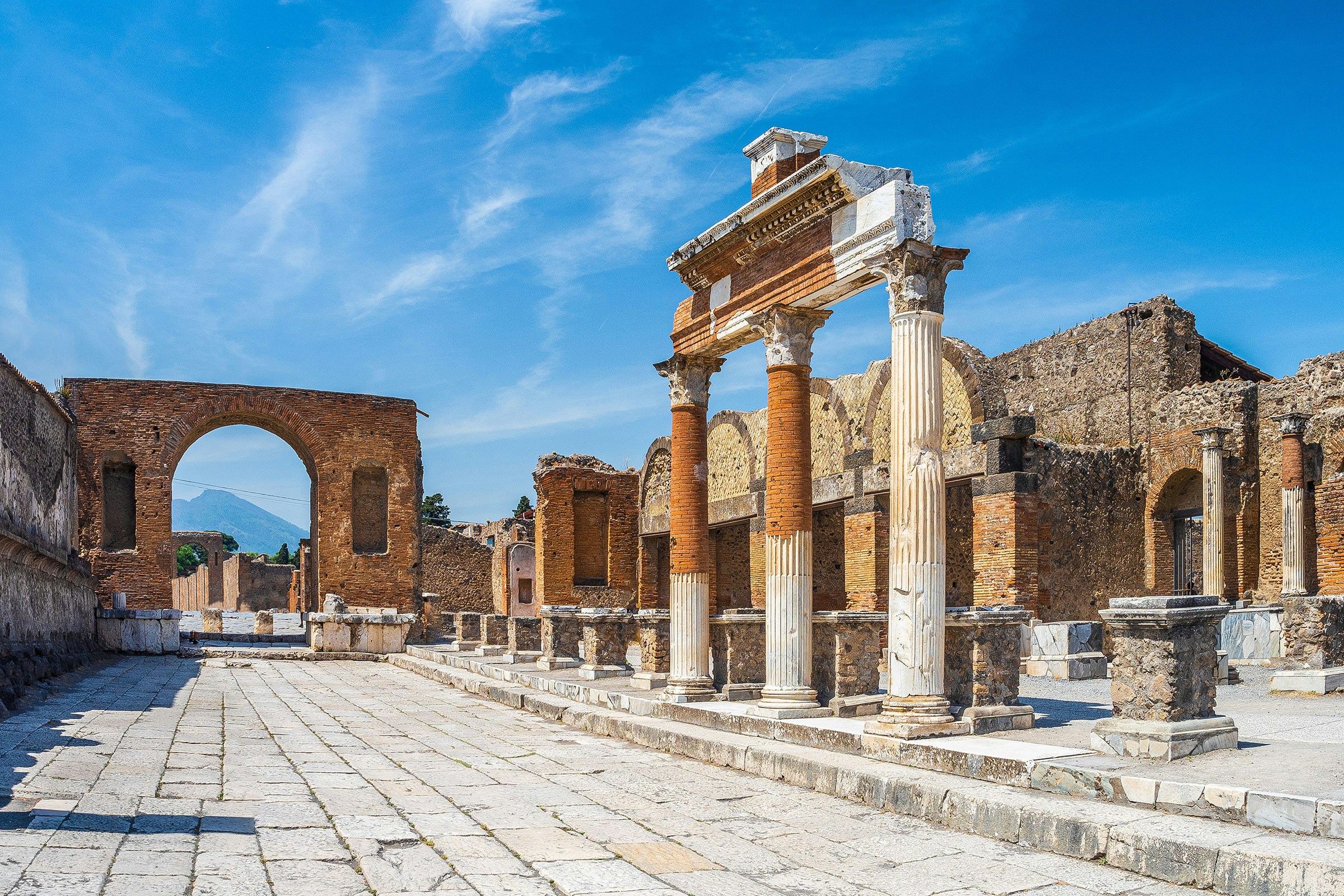 Pompeii Forum ruins with ancient columns and archway under a clear blue sky.