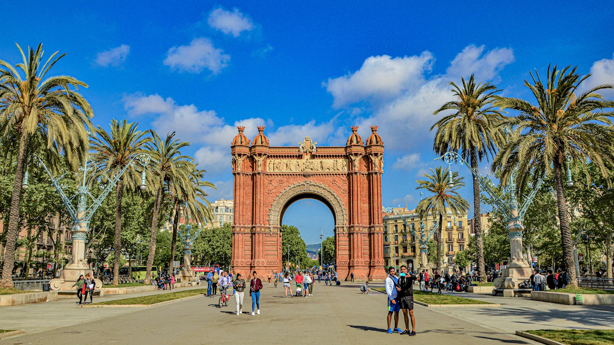 Arc de Triomf in Barcelona with people walking and palm trees lining the path.